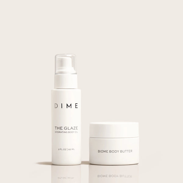 Two white skincare products: a spray bottle labeled "The Glaze Hydrating Body Oil" and a jar labeled "Biome Body Butter."
