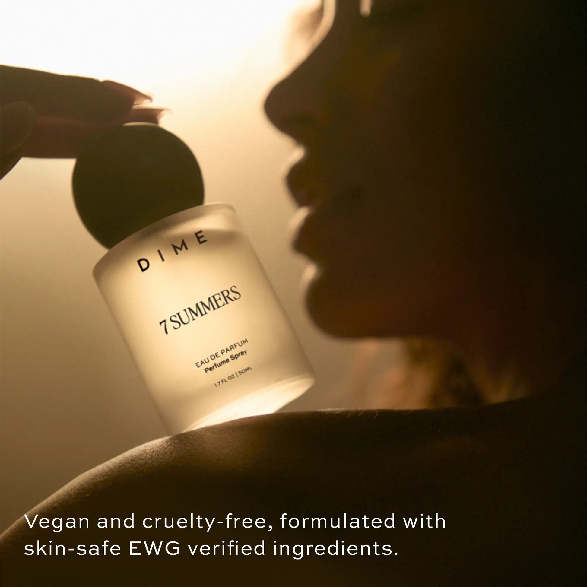 Clear glass perfume bottle labeled "7 Summers" held against a person's face in warm lighting.