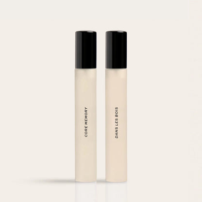 Two tall, slim perfume bottles with cream-colored bodies and black caps labeled "Core Memory" and "Dawns Less Bovis."
