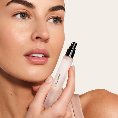 Person holding a white spray bottle with black atomizer labeled "Damselfly Goods" against a neutral background.