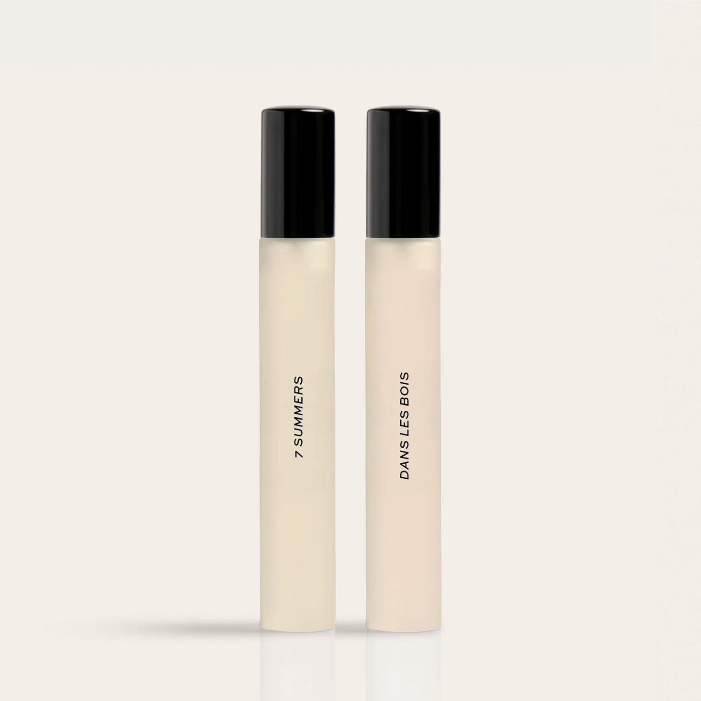 Two cylindrical fragrance bottles with black caps and cream-colored liquid, labeled "7 Summers" and "Damselless Bodies".