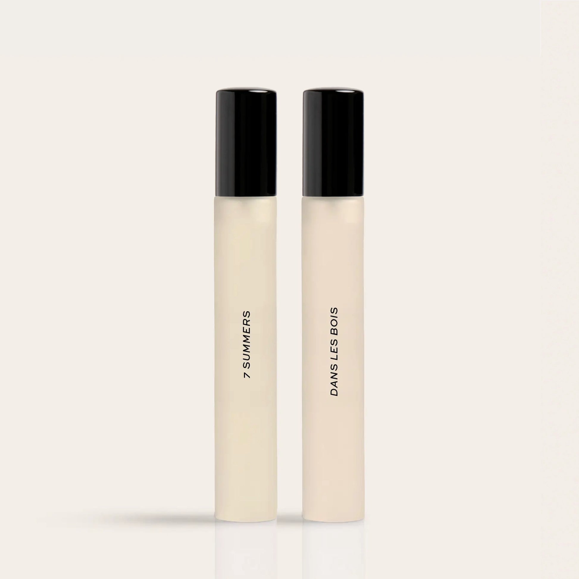 Two cylindrical fragrance bottles with black caps and cream-colored liquid, labeled "7 Summers" and "Damselless Bodies".