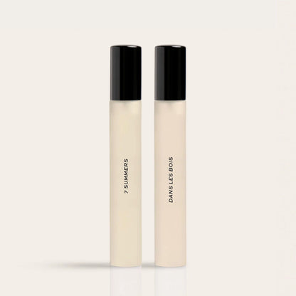 Two cylindrical fragrance bottles with black caps and cream-colored liquid, labeled "7 Summers" and "Damselless Bodies".