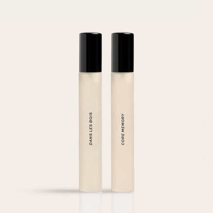 Two cylindrical fragrance bottles with black caps and cream-colored bodies labeled "Dawns Less Bows" and "Core Memory."