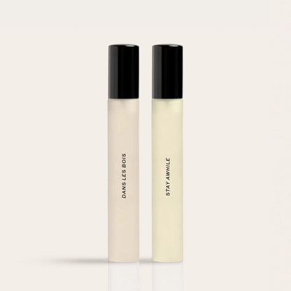 Two slim fragrance bottles with black caps labeled "Daysless Bods" and "Stay Awhile" in cream and pale yellow liquid.