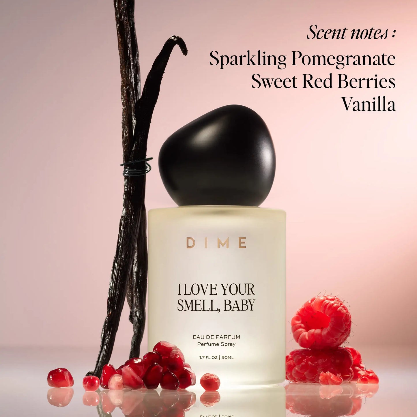Black-capped cream perfume bottle surrounded by vanilla beans and red berries on pink background.
