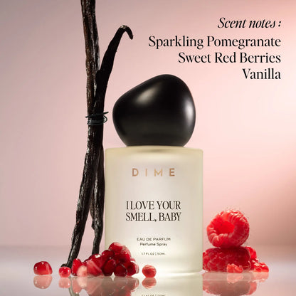 Black-capped cream perfume bottle surrounded by vanilla beans and red berries on pink background.