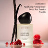 Black-capped cream perfume bottle surrounded by vanilla beans and red berries on pink background.