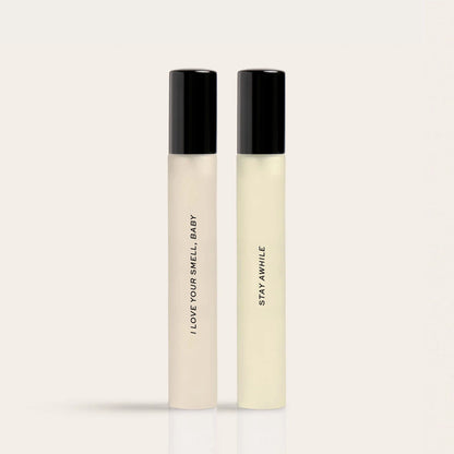 Two rectangular glass bottles with black caps containing light-colored liquid labeled "I Love Your Smell Baby" and "Stay Awhi