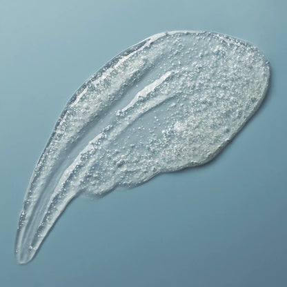 Translucent gel cleanser with visible exfoliating granules in two streaks against a blue background.