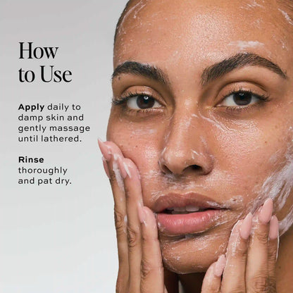 Person with medium skin tone applying lathered cleanser to face with both hands.