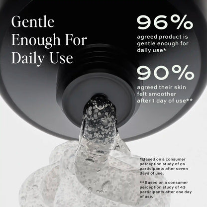 Clear cleanser with exfoliating granules pouring from a dark circular container onto a textured surface.
