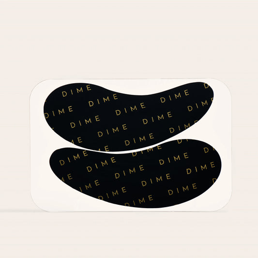 Pair of black curved silicone eye patches with gold "DIME" text pattern throughout.
