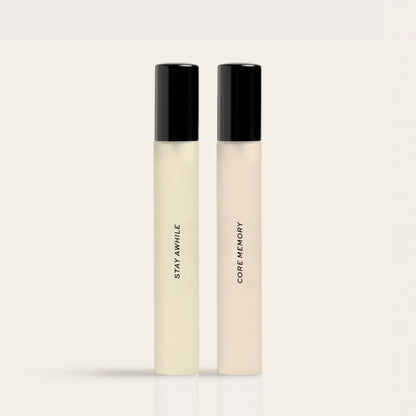 Two rectangular fragrance bottles with black caps; left bottle contains pale yellow liquid labeled "Stay Awhile," right bottl