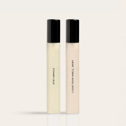 Two cylindrical fragrance bottles with black caps side by side, labeled "Stay Awhile" and "I Love Your Smell Baby".