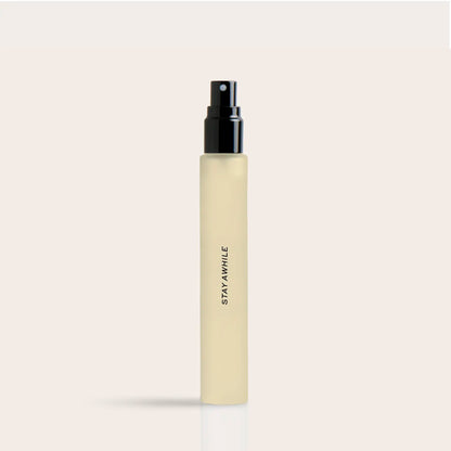 Pale yellow cylindrical spray bottle with black atomizer top and "STAY AWHILE" text on label.