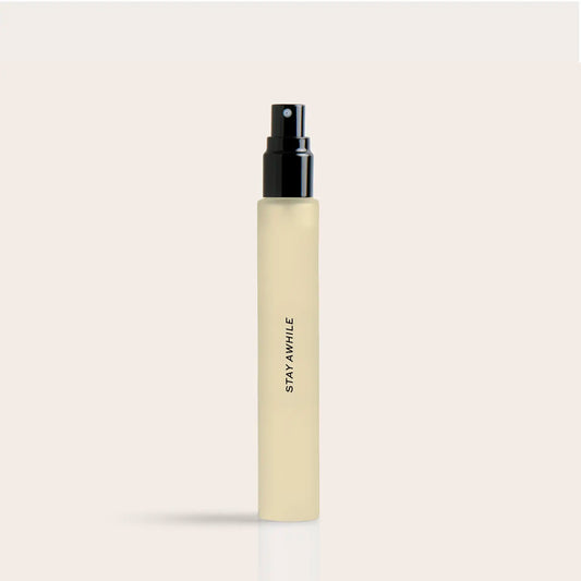 Pale yellow cylindrical spray bottle with black atomizer top and "STAY AWHILE" text on label.