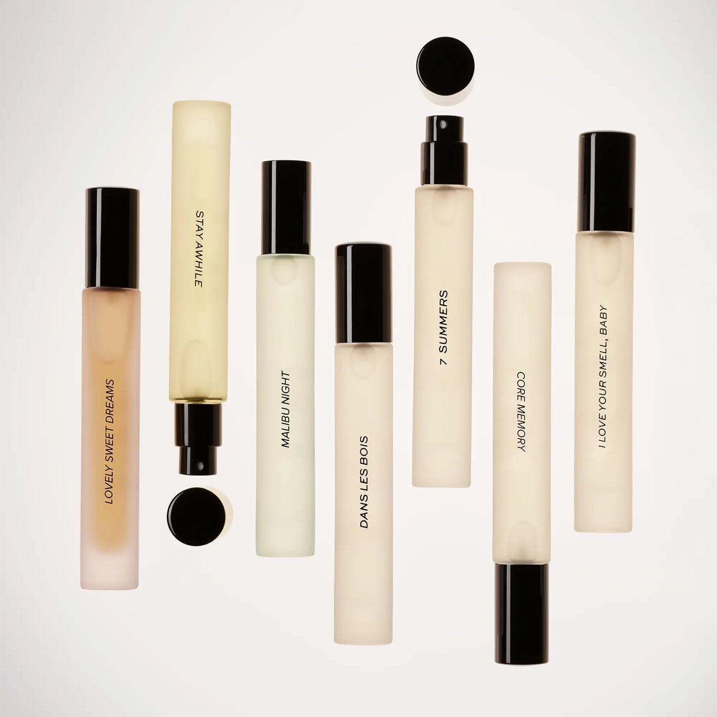 Small cylindrical perfume bottles with black caps in cream and pale gold liquid, arranged in rows against white background.