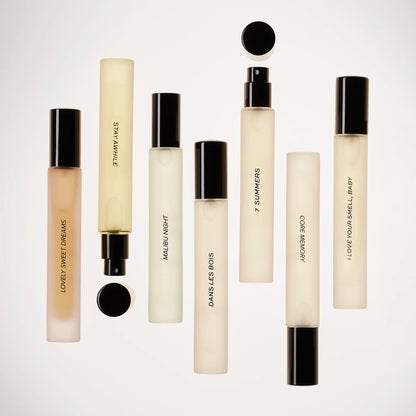 Small cylindrical perfume bottles with black caps in cream and pale gold liquid, arranged in rows against white background.